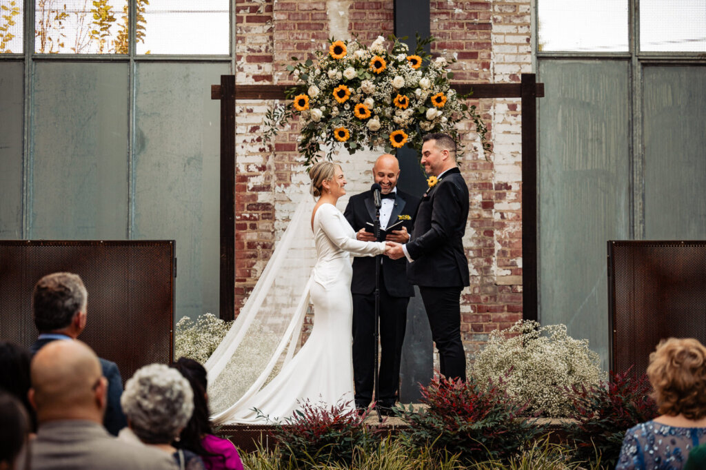 Bride and groom smiling at each other as they hold hands during their wedding ceremony on the altar.