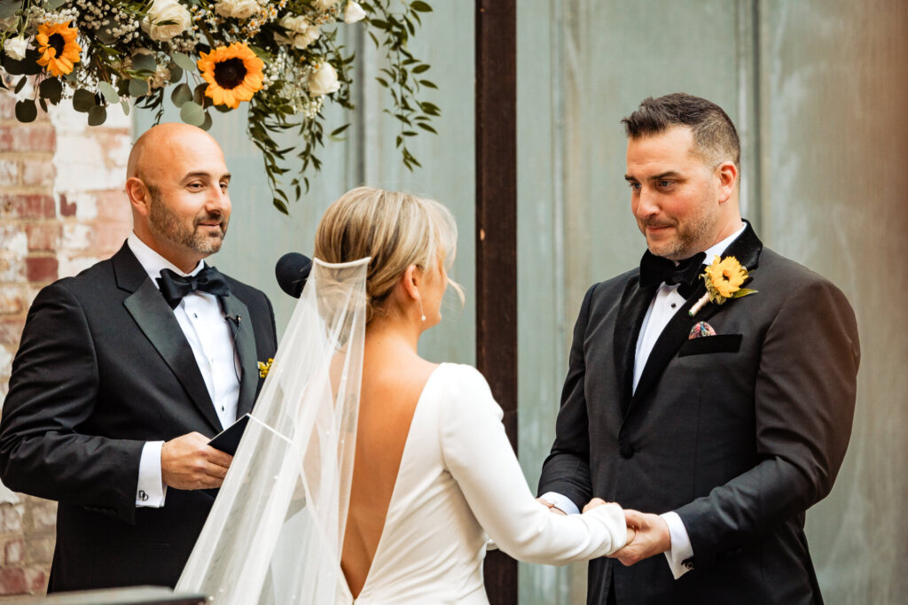 Bride and groom holding hands, smiling at each other during their wedding ceremony