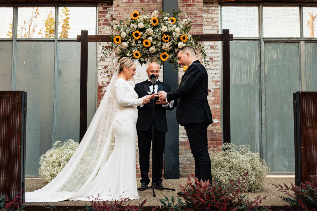 Bride and groom exchanging rings as they stand at the altar, with the officiant in the background.
