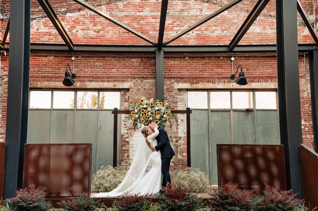 Bride and groom sharing a kiss after exchanging vows, with a floral arch and a beautiful ceremony setting.