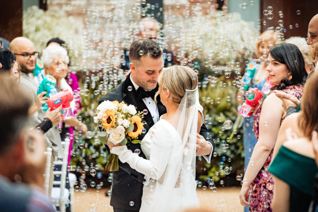 Bride and groom walking down the aisle after the ceremony, surrounded by bubbles and joyful guests