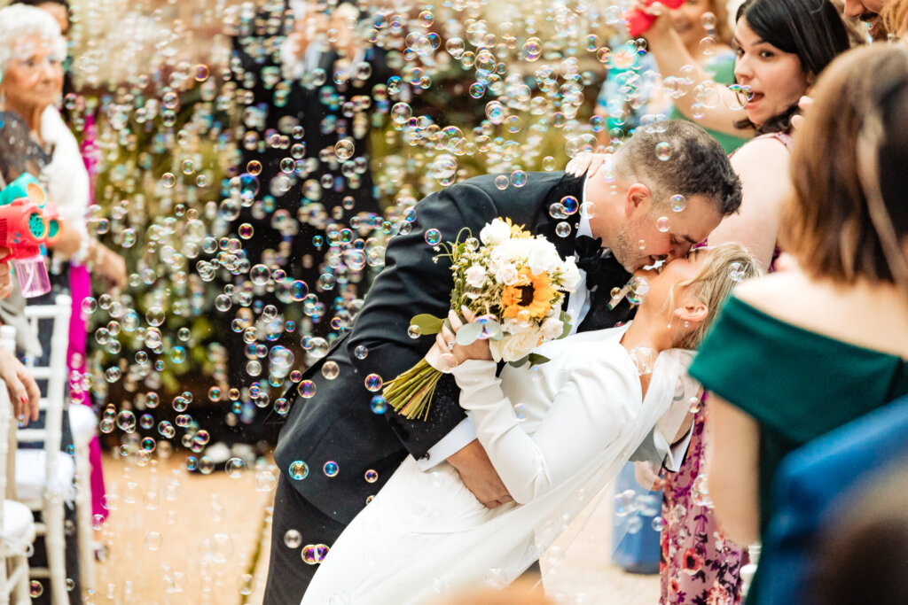 Bride and groom smiling and holding each other close as bubbles float around them after the ceremony.