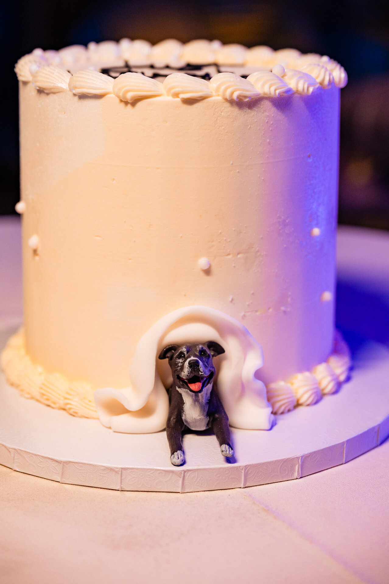 Wedding cake featuring a dog figurine sitting at the base, wrapped in fondant for a unique and personal touch.