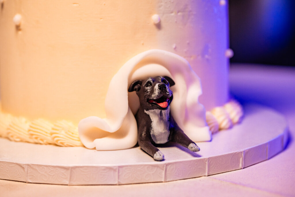Close-up of the wedding cake featuring a dog figurine wrapped in fondant, sitting at the base of the cake