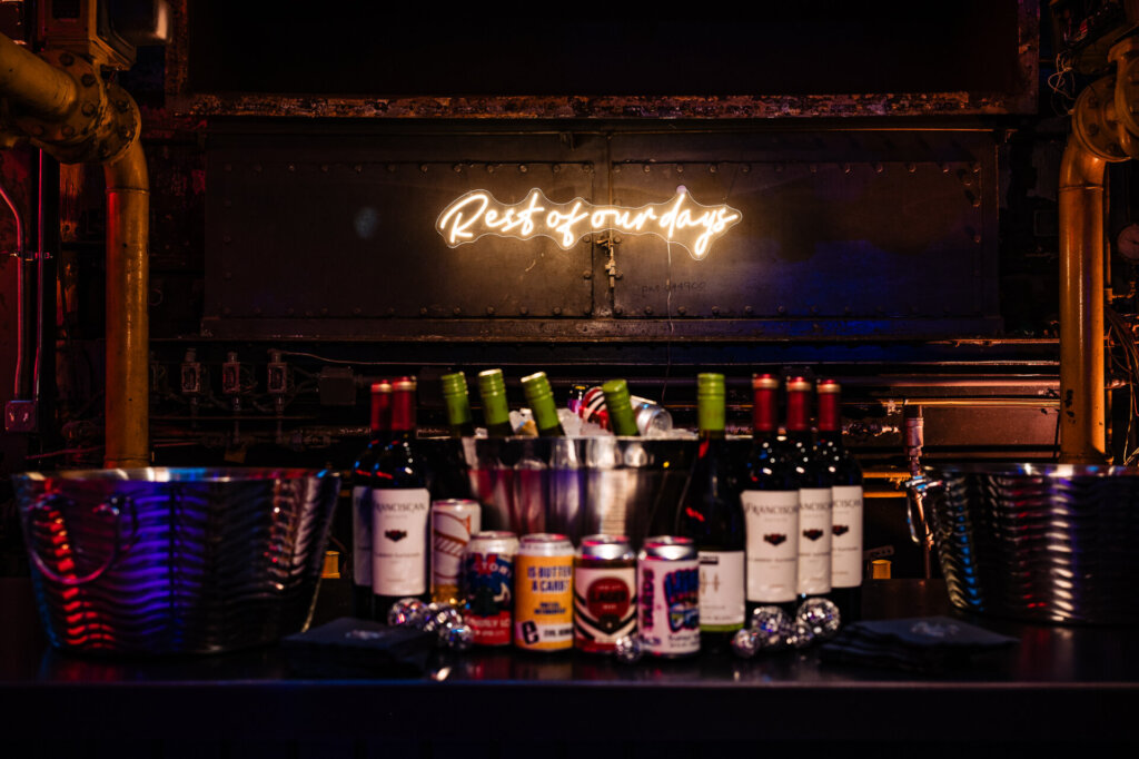 Bar area with a neon sign reading 'Rest of our days' and various bottles and cans lined up for the wedding reception.