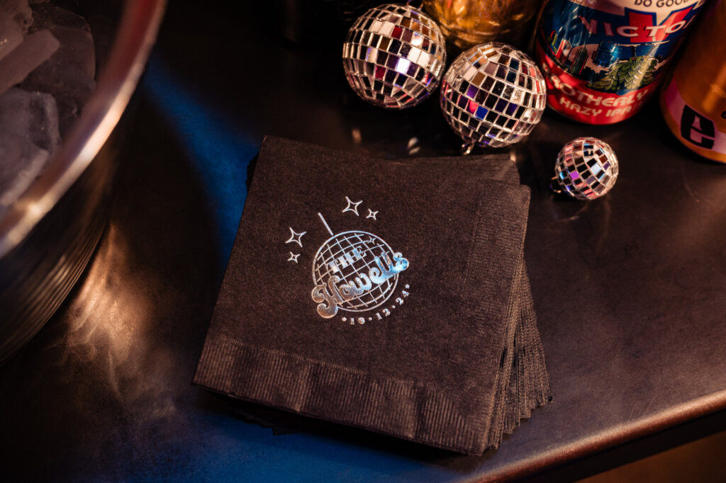 Wedding reception details with branded napkins, disco ball decor, and beverage cans on a table