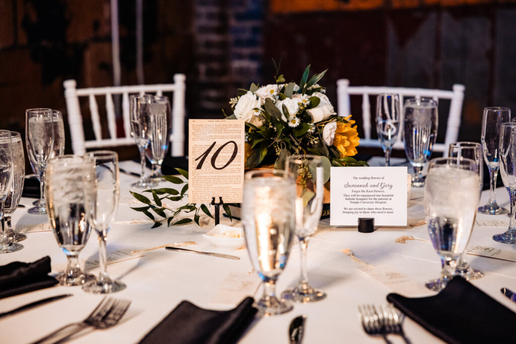 Wedding reception table with a centerpiece of flowers and a table number card, surrounded by elegant glassware.