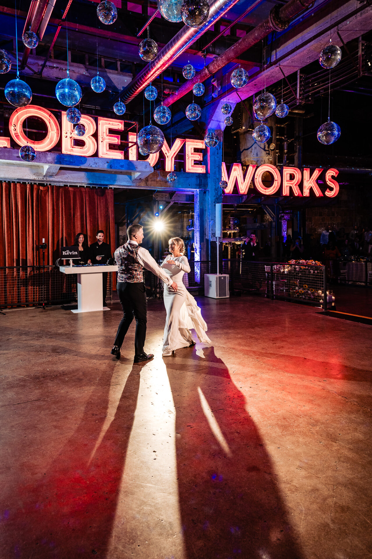 Bride and groom dancing on the floor, with colorful lights and the 'GLOBE DYE WORKS' sign in the background