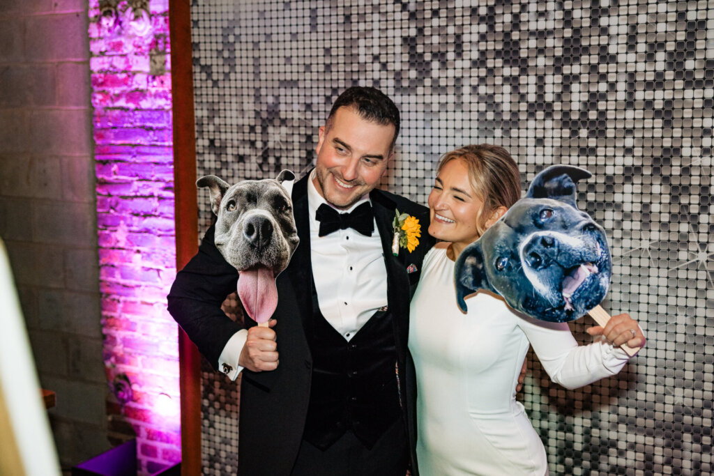 Bride and groom smiling and holding their dog while posing with disco balls, captured in front of a stylish backdrop