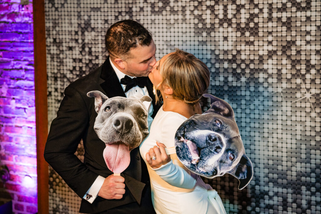 Bride and groom sharing a kiss while holding their dog, with a disco ball prop on the groom's shoulder
