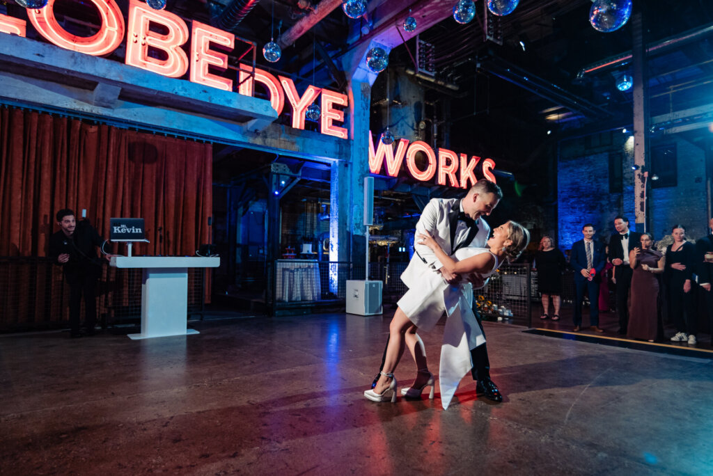 Bride and groom dancing energetically on the reception dance floor with colorful lighting.