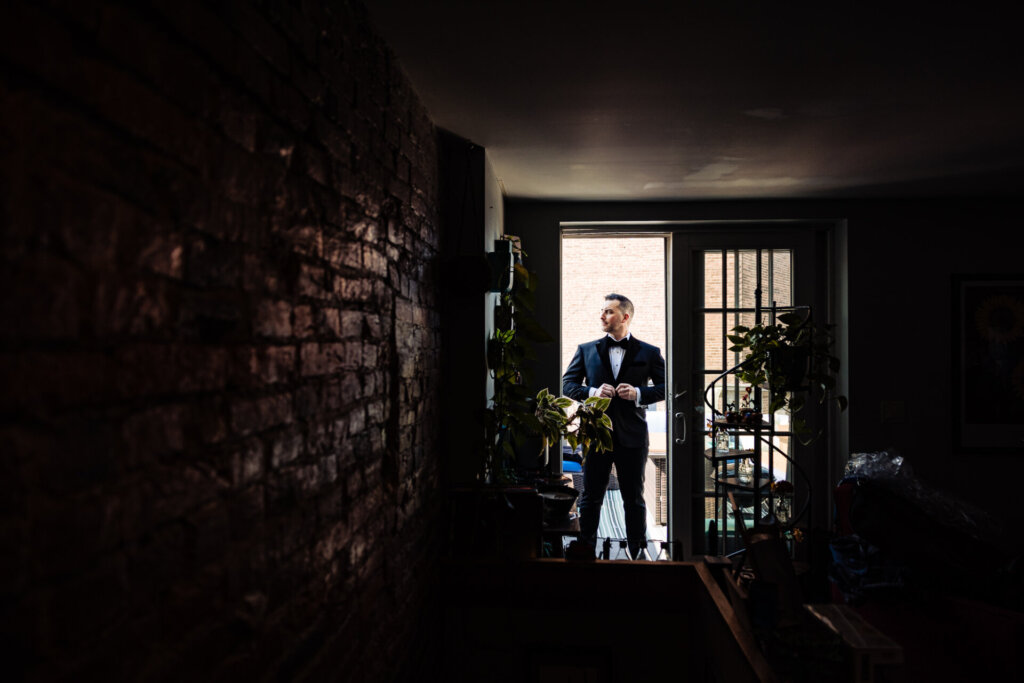 Groom standing in a doorway, confidently posing in his wedding suit.