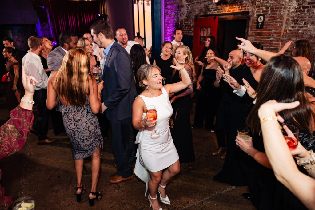 Guests having fun and dancing at the wedding, with the bride in a white dress among the crowd.
