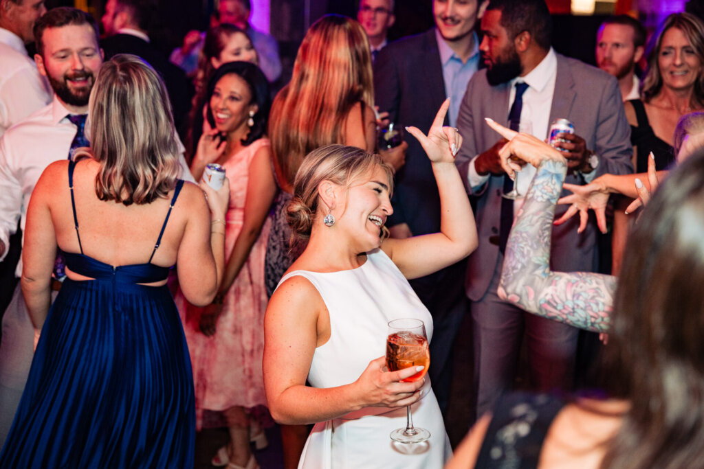 Bride and guests enjoying the dance floor, celebrating together with drinks in hand.