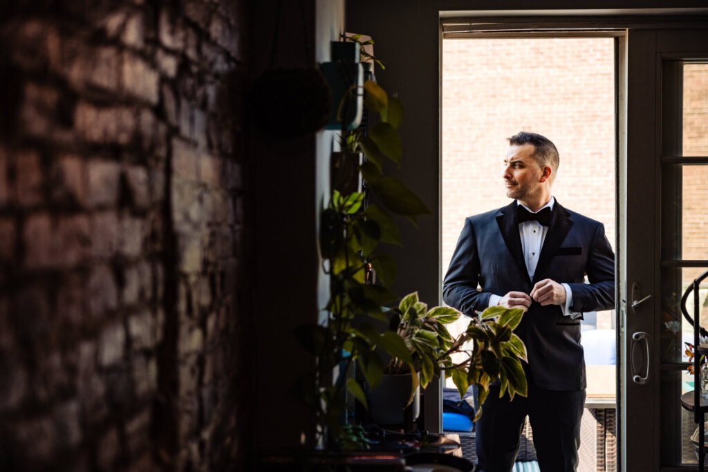 Groom standing in the doorway, confidently posing in his wedding suit.
