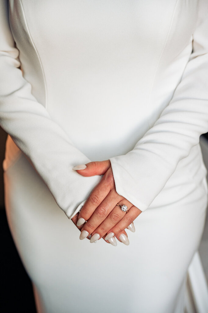 Close-up shot of the bride's hands highlighting her manicured nails, the cuffs of her long-sleeve gown, and her wedding ring
