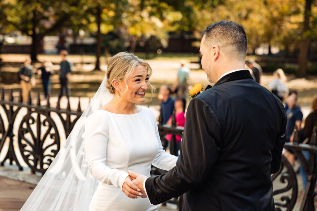 Bride smiling as she faces the groom during their first look, capturing a joyful moment.