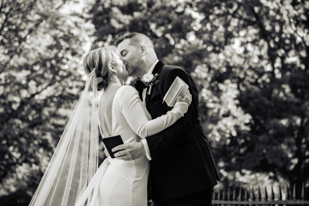 Black and white shot of the bride and groom sealing their first look moment with a sweet kiss.