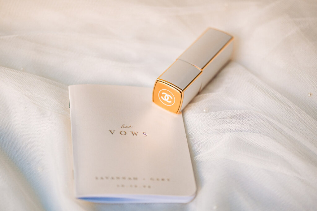 legant bridal booklet placed beside a white Chanel lipstick on a soft fabric background.