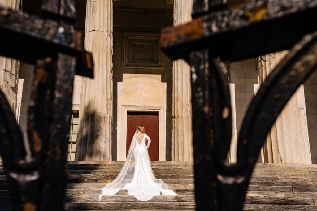 Wide shot of the bride's back as she ascends the staircase, with her gown trailing elegantly behind her.