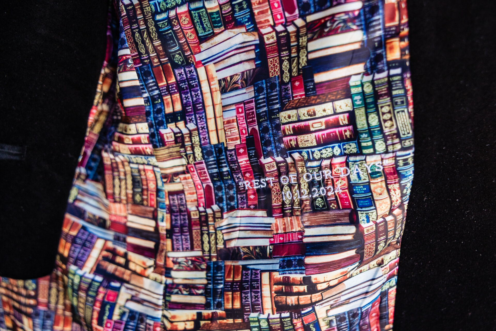 Close-up of a colorful book-patterned fabric lining inside a jacket with the embroidered text 'Rest of Our Days 10-12-2024.