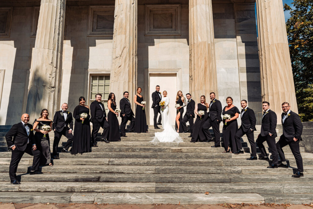Bride and groom standing at the top of the staircase, with bridesmaids and groomsmen posing on the steps below them