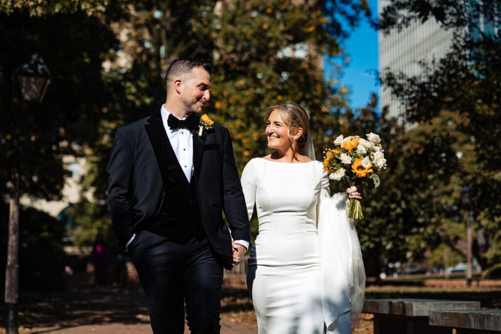 Bride and groom looking at each other lovingly as they walk together through a beautiful natural setting.