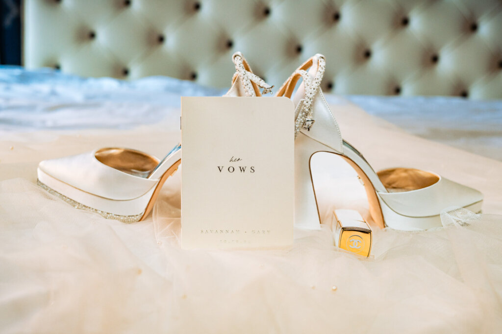 Bridal booklet placed alongside a white Chanel lipstick leaning on her wedding white platform heels.
