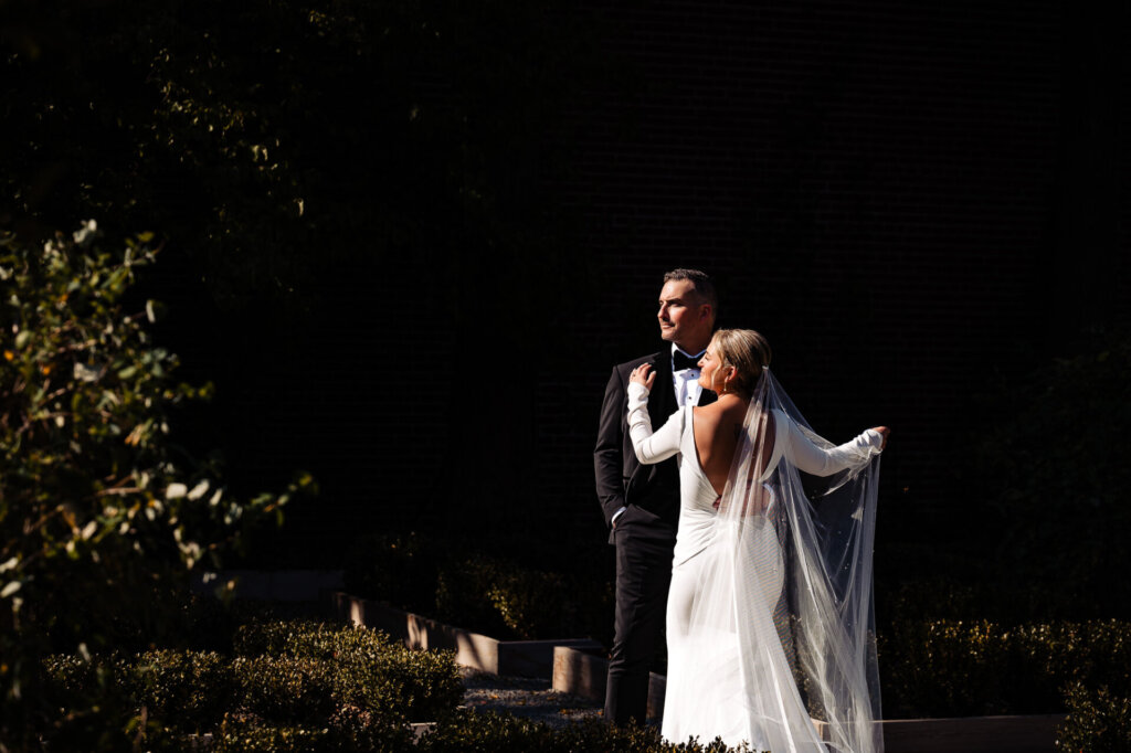 Wide shot of the bride and groom posing together in the shadows of nature, with soft light filtering through the trees.
