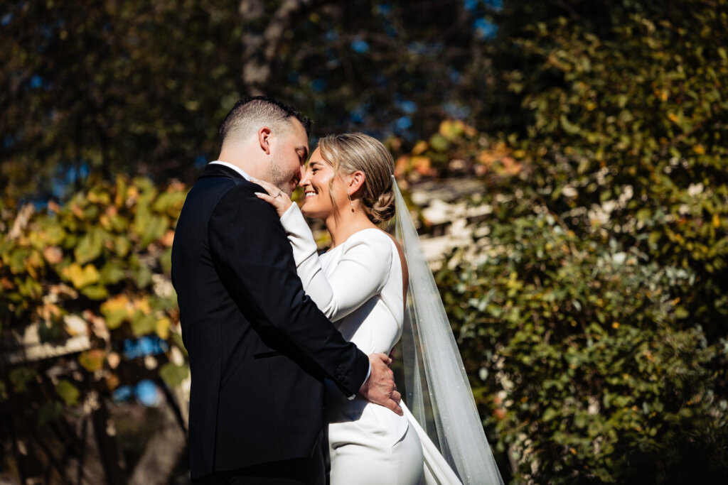 Bride and groom smiling while gently leaning their foreheads together in a loving embrace.