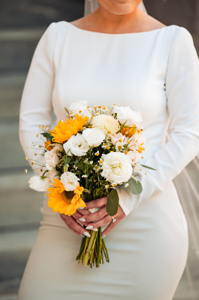 Bride holding a vibrant bouquet of white and yellow flowers, standing gracefully.
