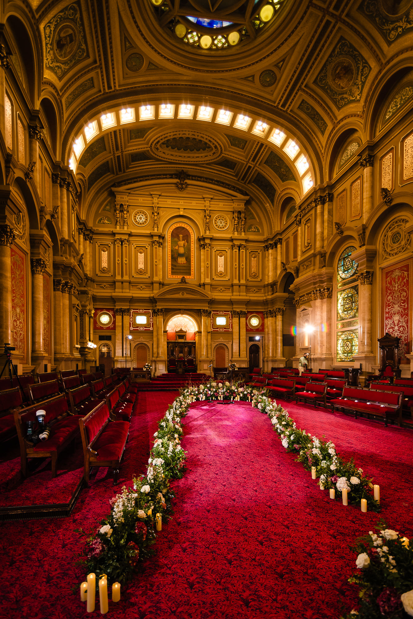 Red-carpeted wedding aisle lined with flowers and candles in an ornate ceremony hall