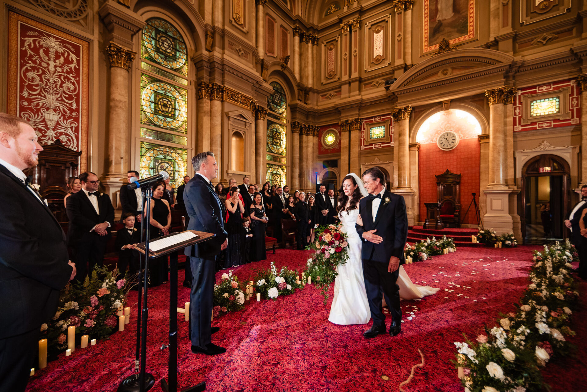 Bride's father walking her down the aisle together, smiling as guests watch