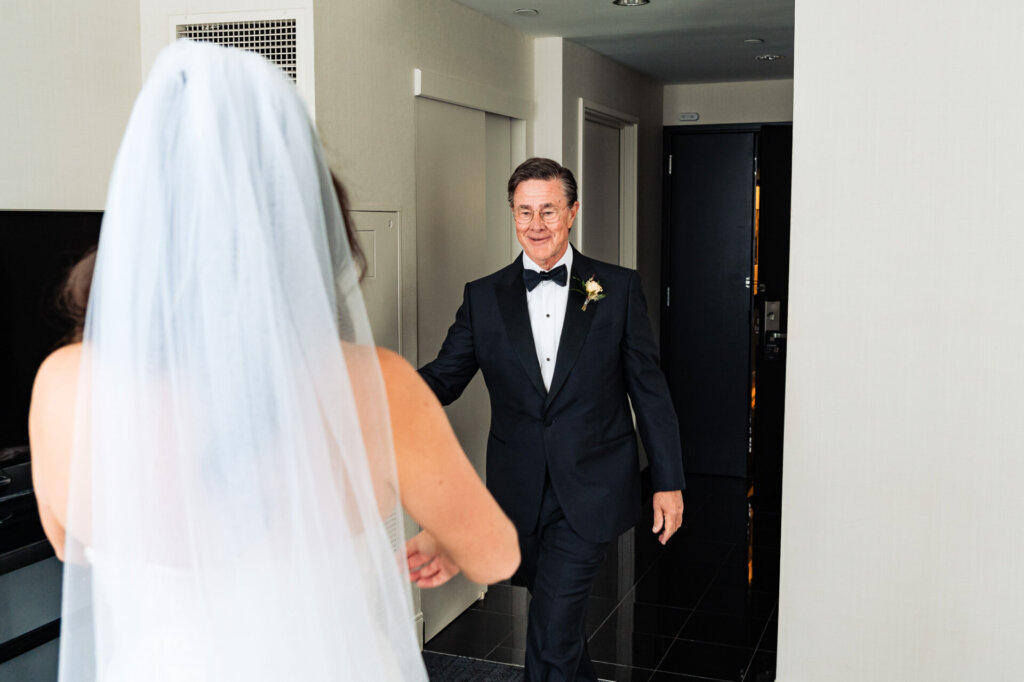 Bride walking towards her father with a radiant smile, wearing a flowing veil and white wedding gown