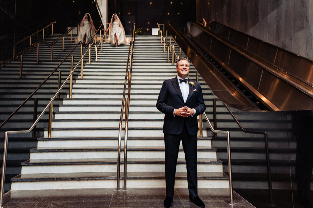 Bride approaching groom during their first look at the bottom of the staircase