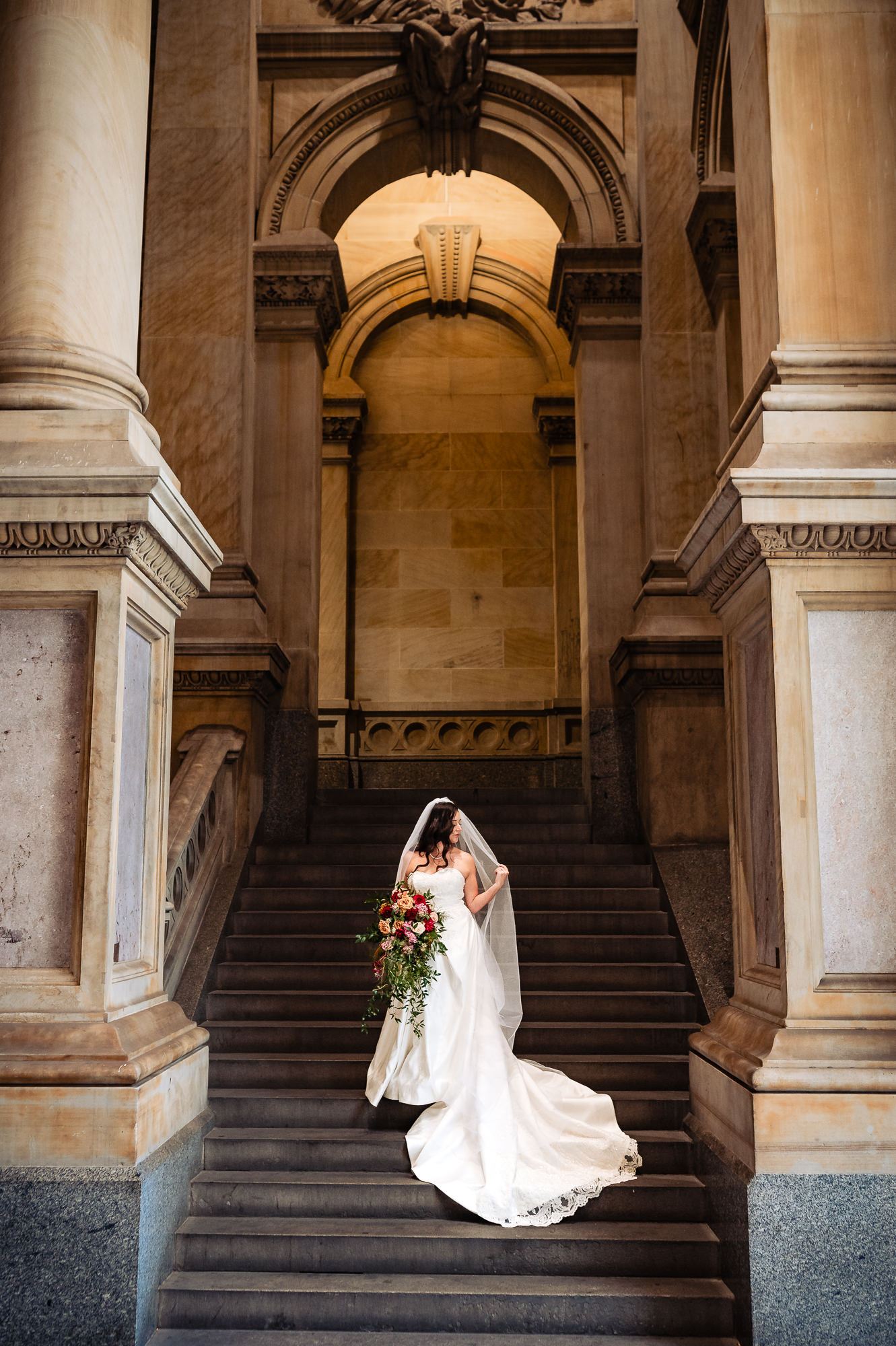 Bride posing on historic stone steps, holding a cascading bouquet of flowers
