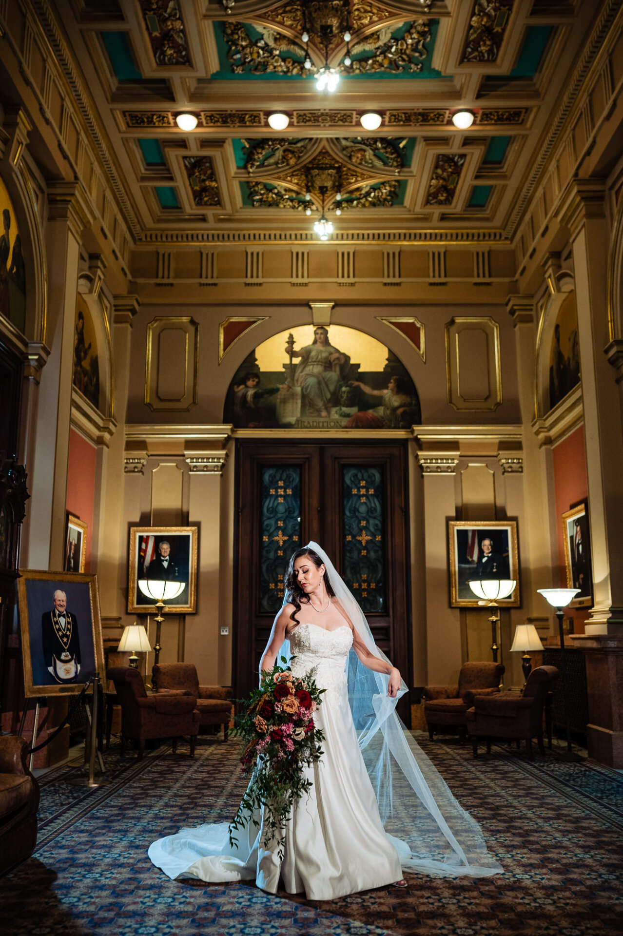 Bride posing in an ornate room, holding her bouquet and veil with elegance