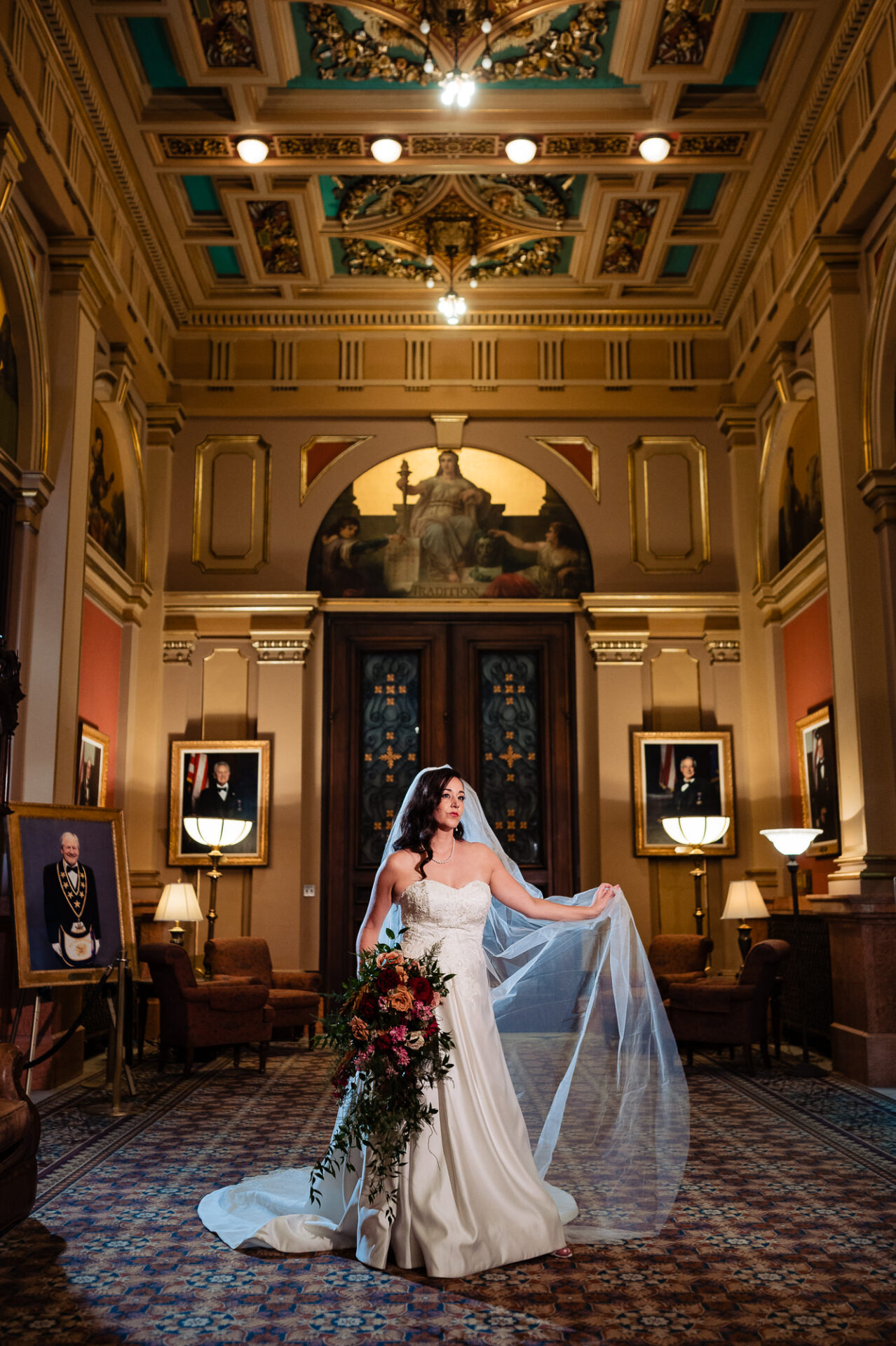Bride standing in the center of an opulent room, holding her bouquet and looking to the side