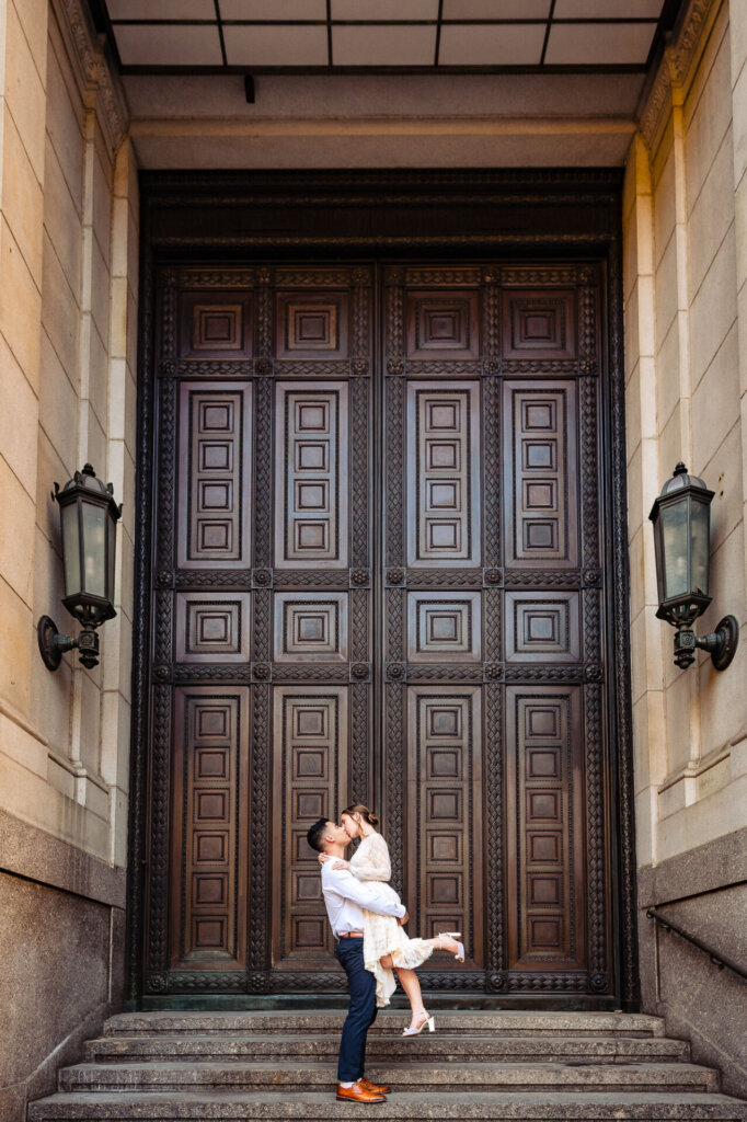 Batsheva and Josh kissing in front of a large ornate wooden door with symmetrical lanterns on either side.