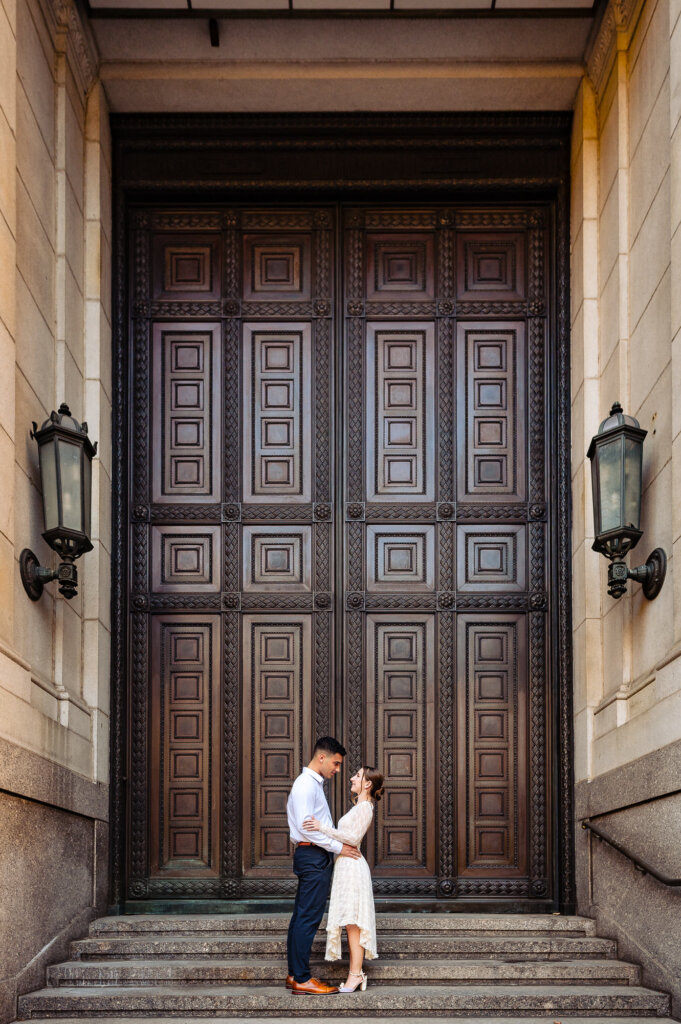 A full-length view of Batsheva and Josh in front of the same grand door, embracing each other.
