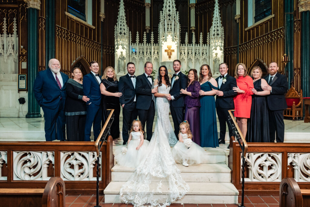 Bride and groom standing with a mixed group of family members, including seated loved ones, in front of the cathedral’s detailed altar.