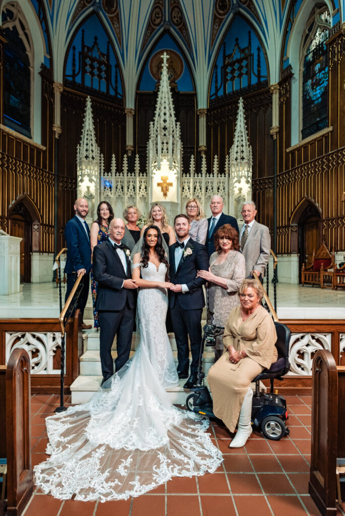 Bride and groom posing with extended family members, including seated relatives, on the church altar steps, with the ornate backdrop adding grandeur.