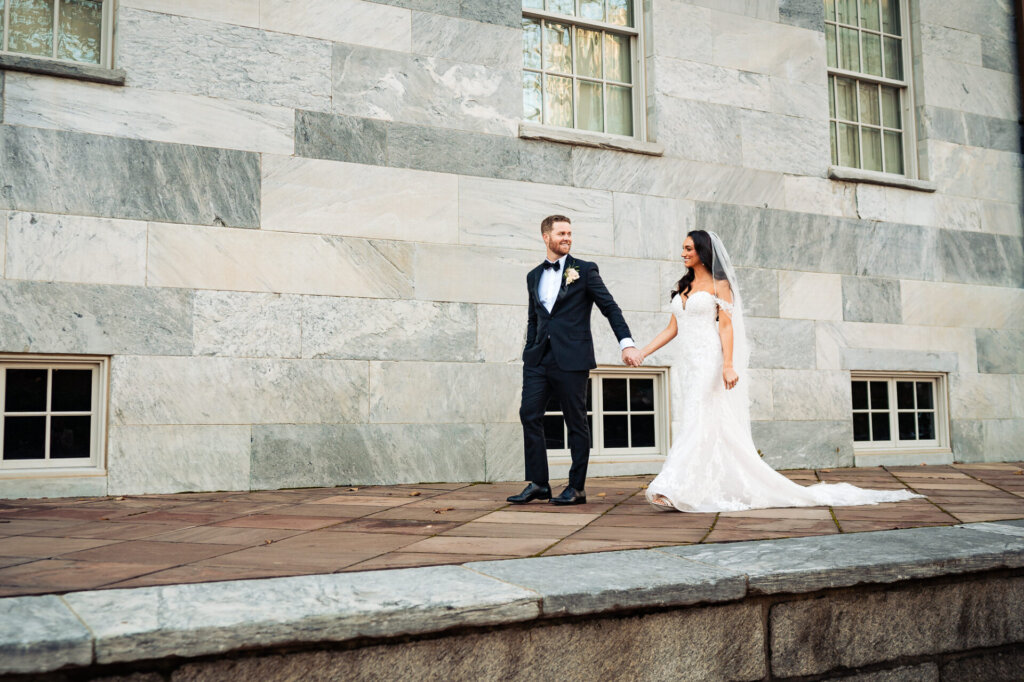 Bride and groom walking together along a stone pathway, the bride’s lace gown and veil adding elegance to the setting.