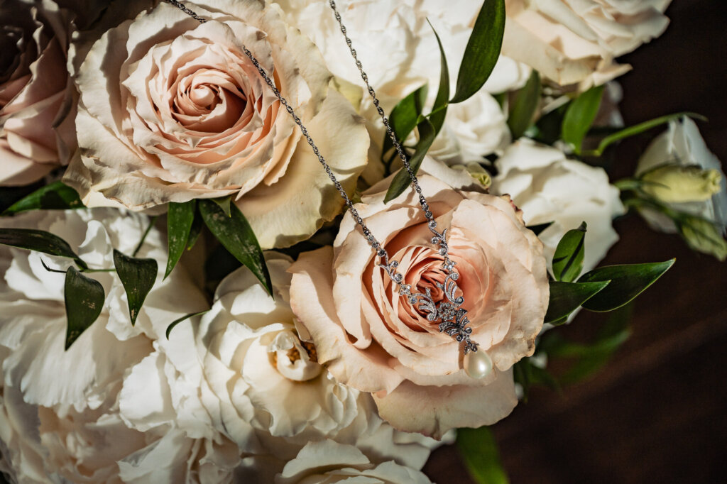 Wedding bouquet featuring pale pink and cream roses, white florals, and lush greenery with subtle dewdrop details.