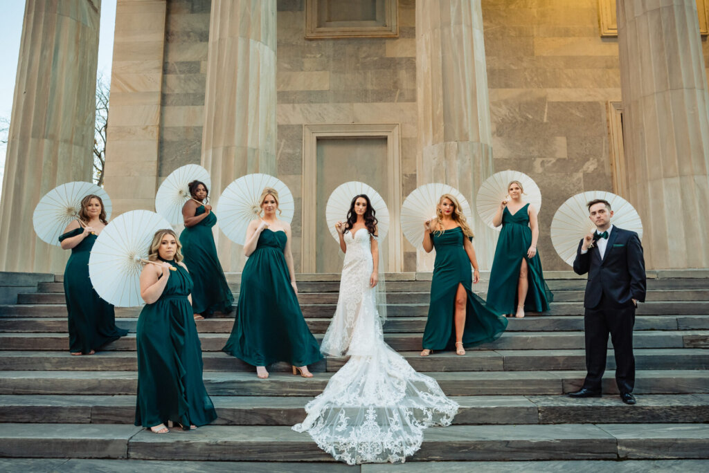 Bridal party members posing with parasols, complementing their emerald green dresses and elegant poses on the steps.