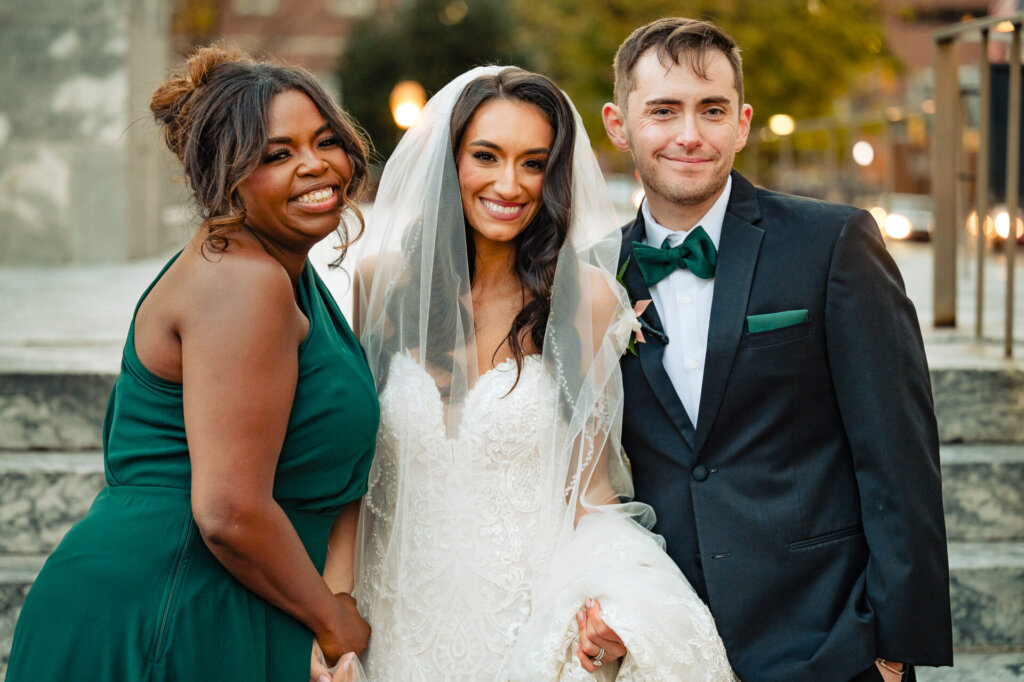 Bride posing with two members of the bridal party, their cheerful expressions set against an outdoor backdrop
