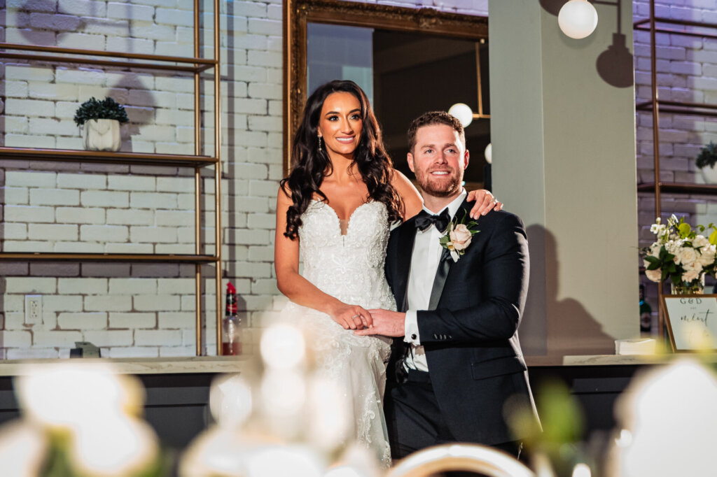 Bride and groom seated at the reception, smiling warmly as they pose together in front of the beautifully decorated venue backdrop.