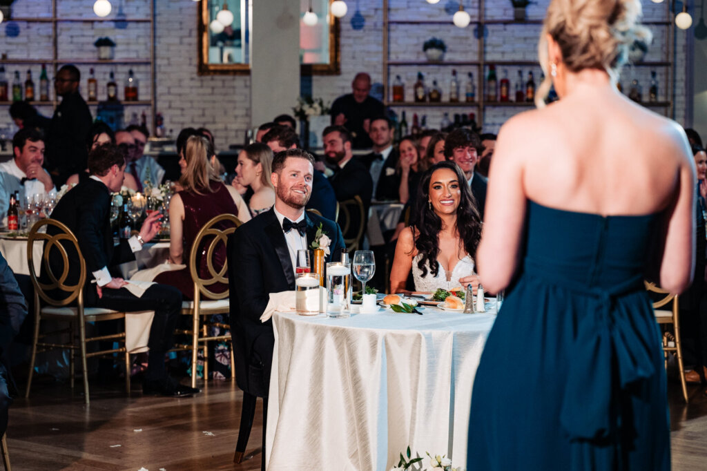 Another bridesmaid in an elegant dress giving a speech while standing in front of the seated couple.