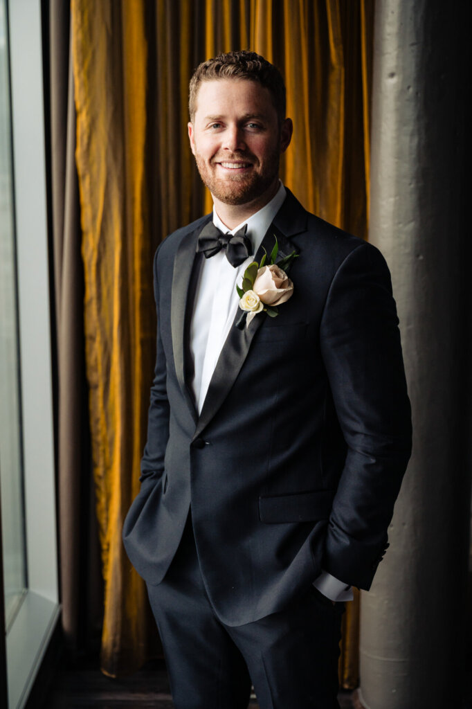 Groom smiling warmly in his tuxedo, his boutonniere adding a touch of elegance to the outfit.