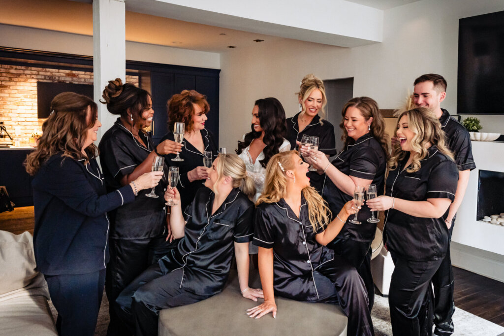 Bridal party cheering with champagne glasses in hand, dressed in matching satin robes, celebrating in a cozy and elegant living room.
